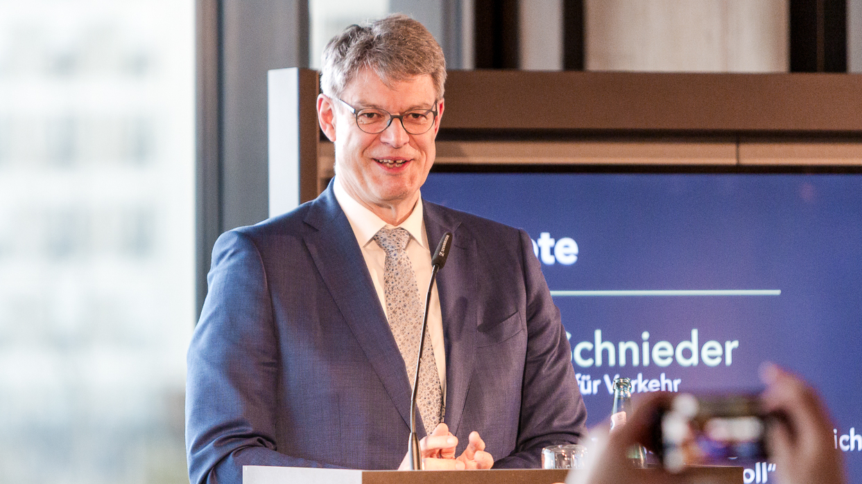A man in a suit speaks at a podium with 'Circle C' logo, audience members capture the moment on phones.