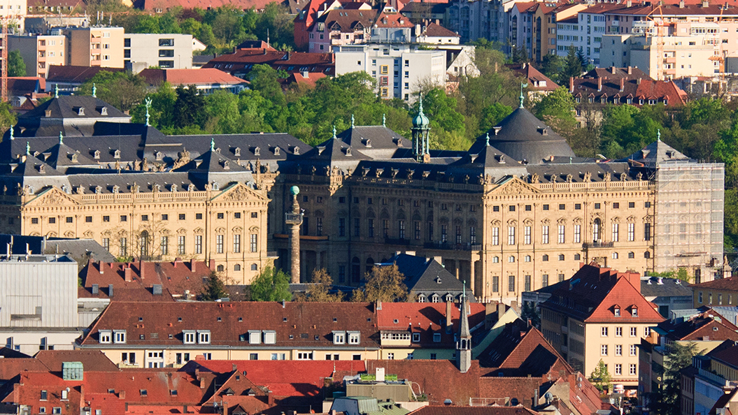 Cityscape of Würzburg, Germany, featuring the large historic building of Würzburg Residence surrounded by red rooftops and greenery.