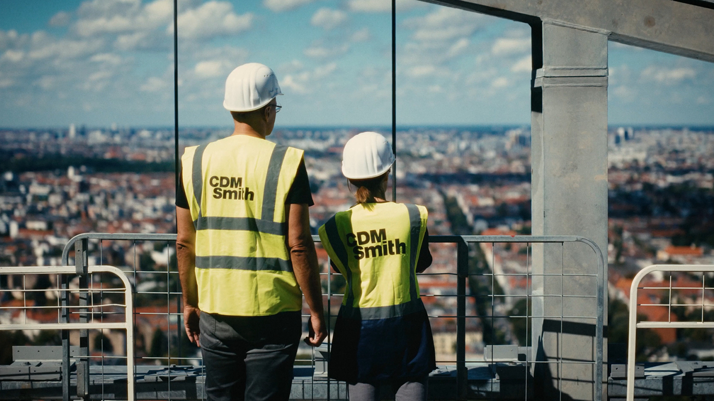 Two construction workers in safety gear overlooking a city skyline.