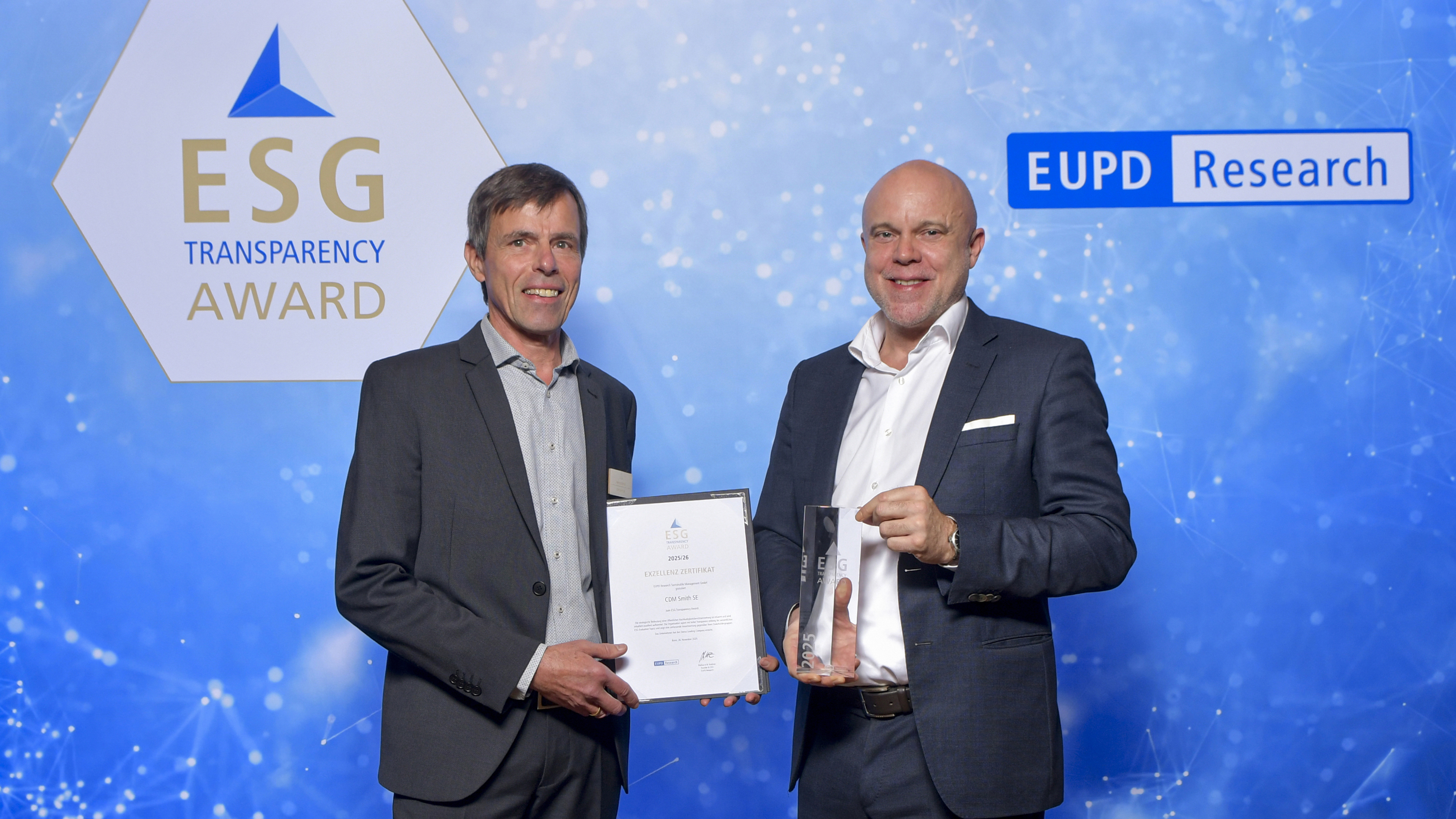 Two people in suits, holding the ESG Transparency Award and a certificate, standing in front of a blue background.