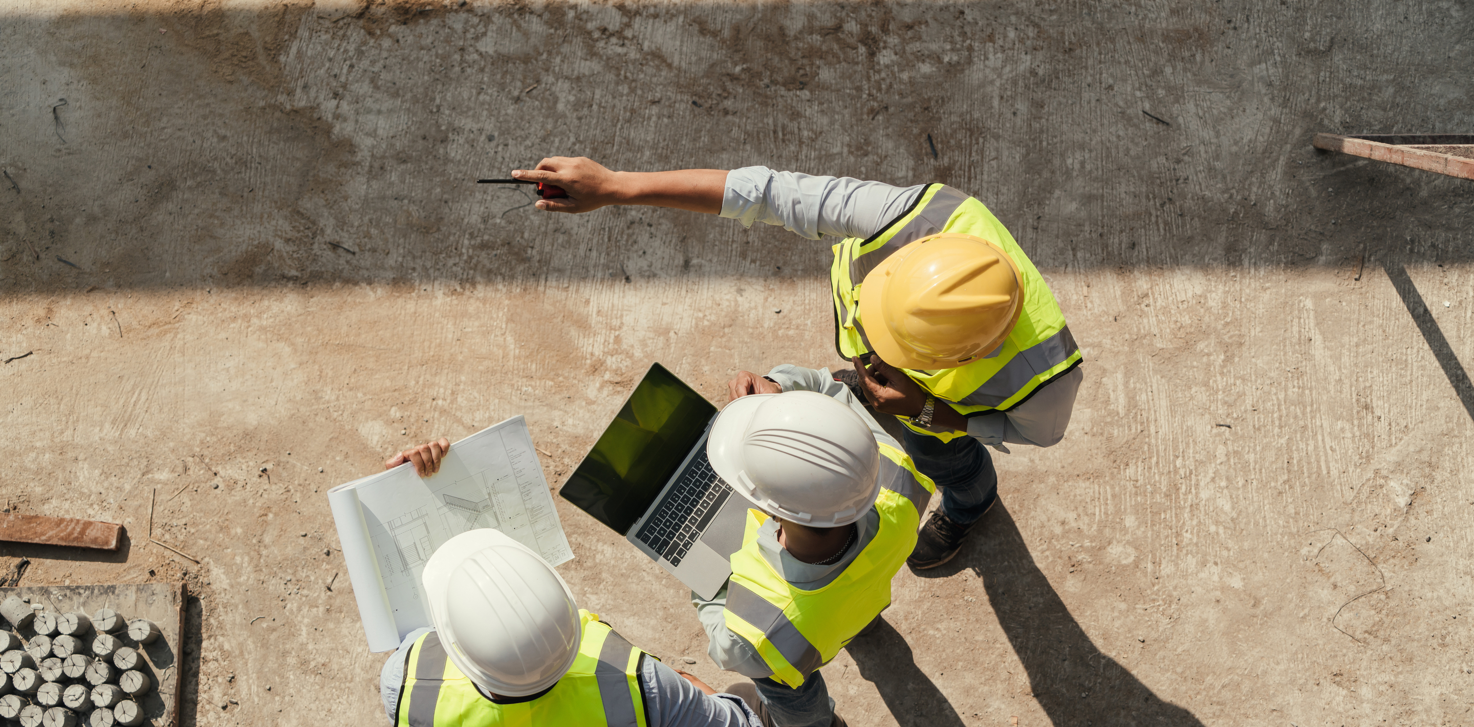 Drei Bauingenieur*innen mit Schutzkleidung überwachen die Baustelle