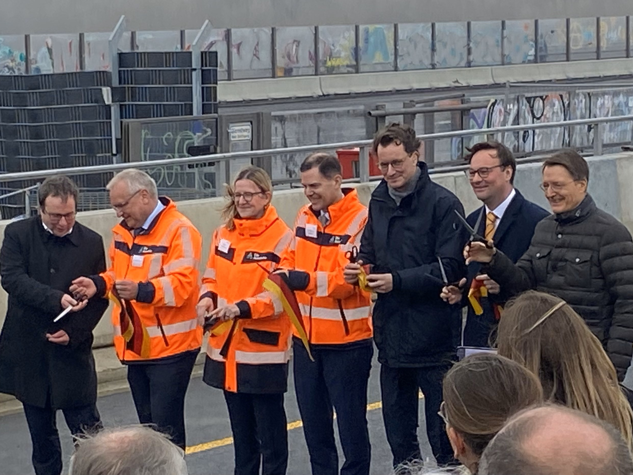 Group of people in safety vests at a ribbon-cutting event on a bridge.