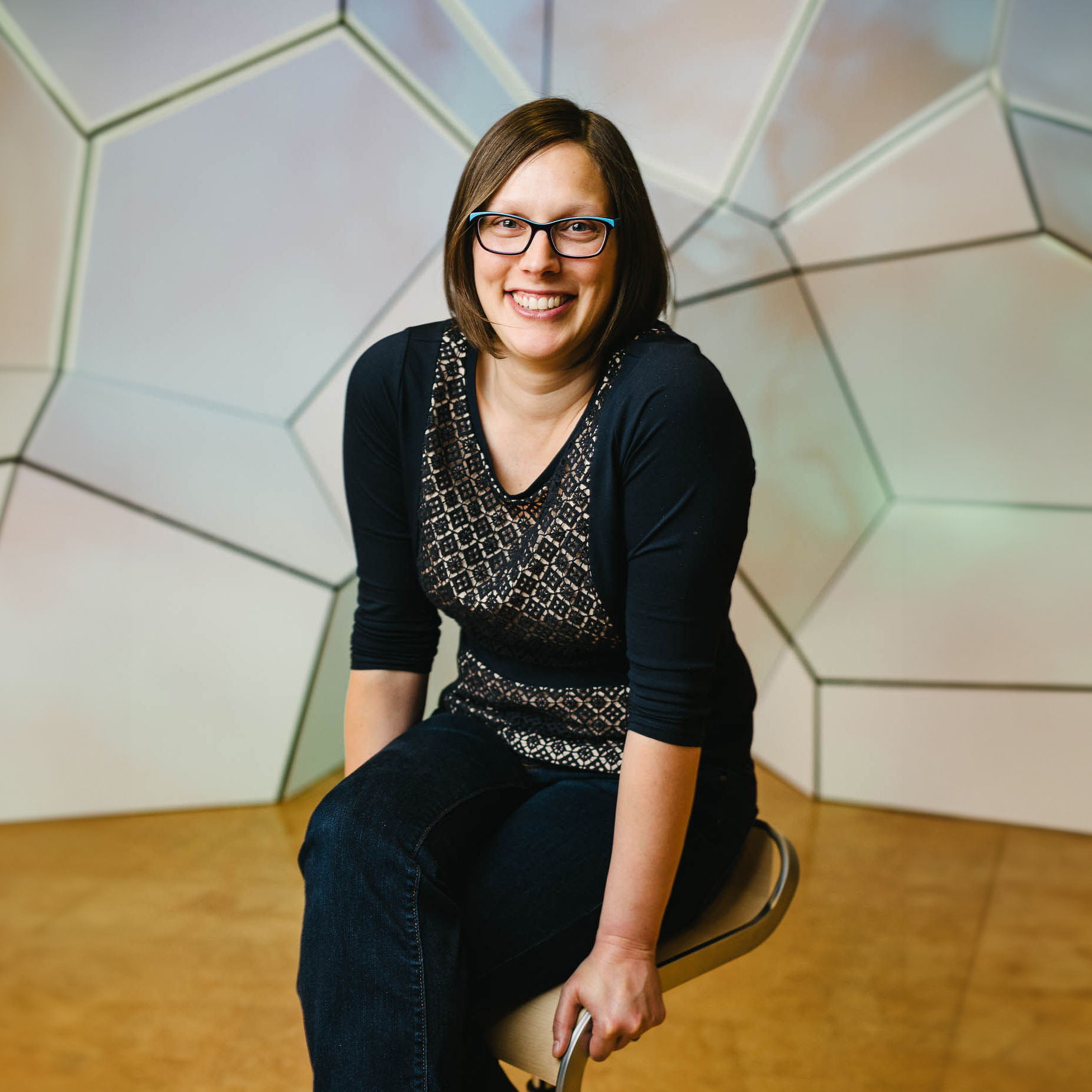 Person seated on a stool in front of a geometric wall.