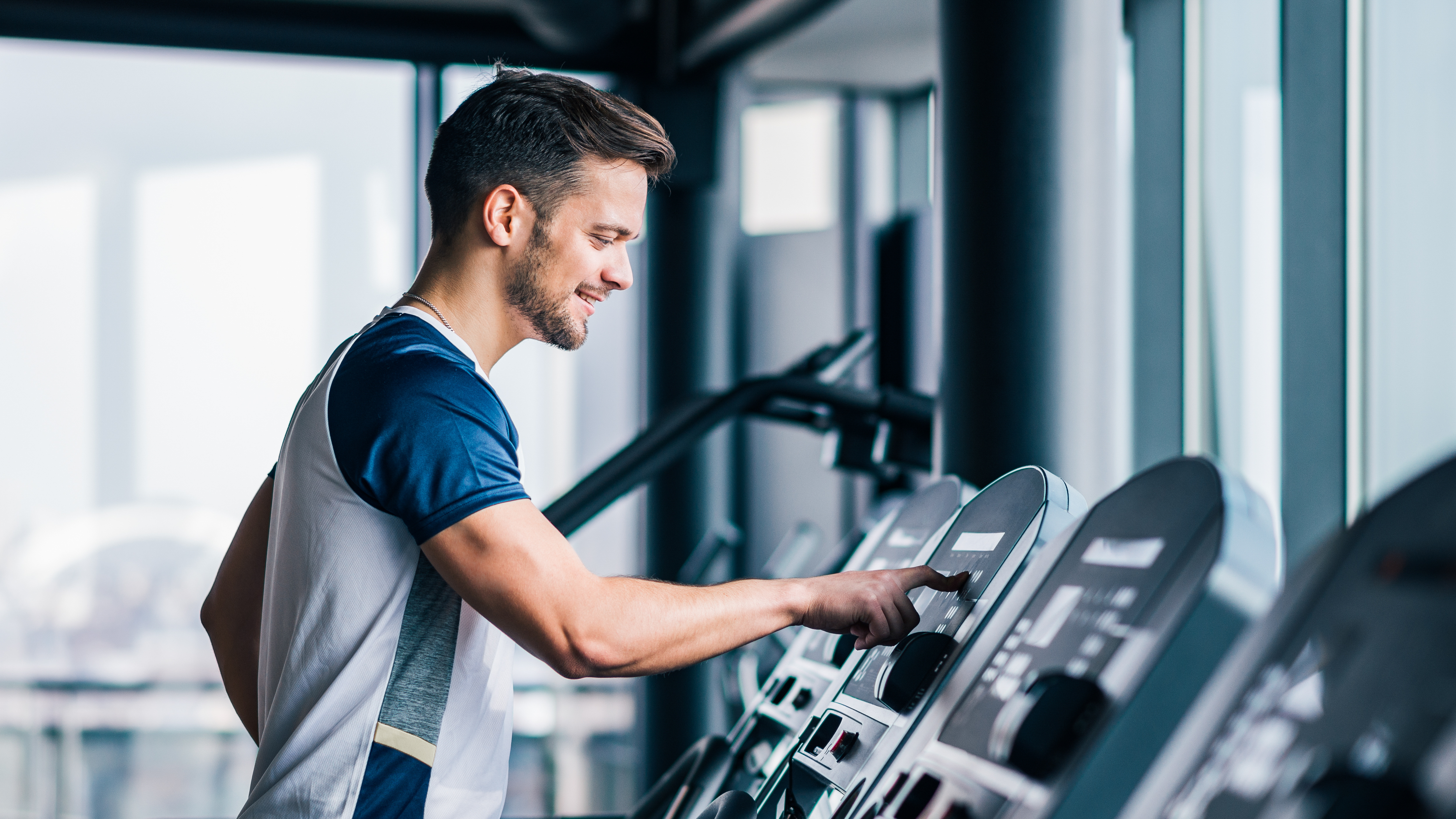 Person using a treadmill in a gym with large windows.