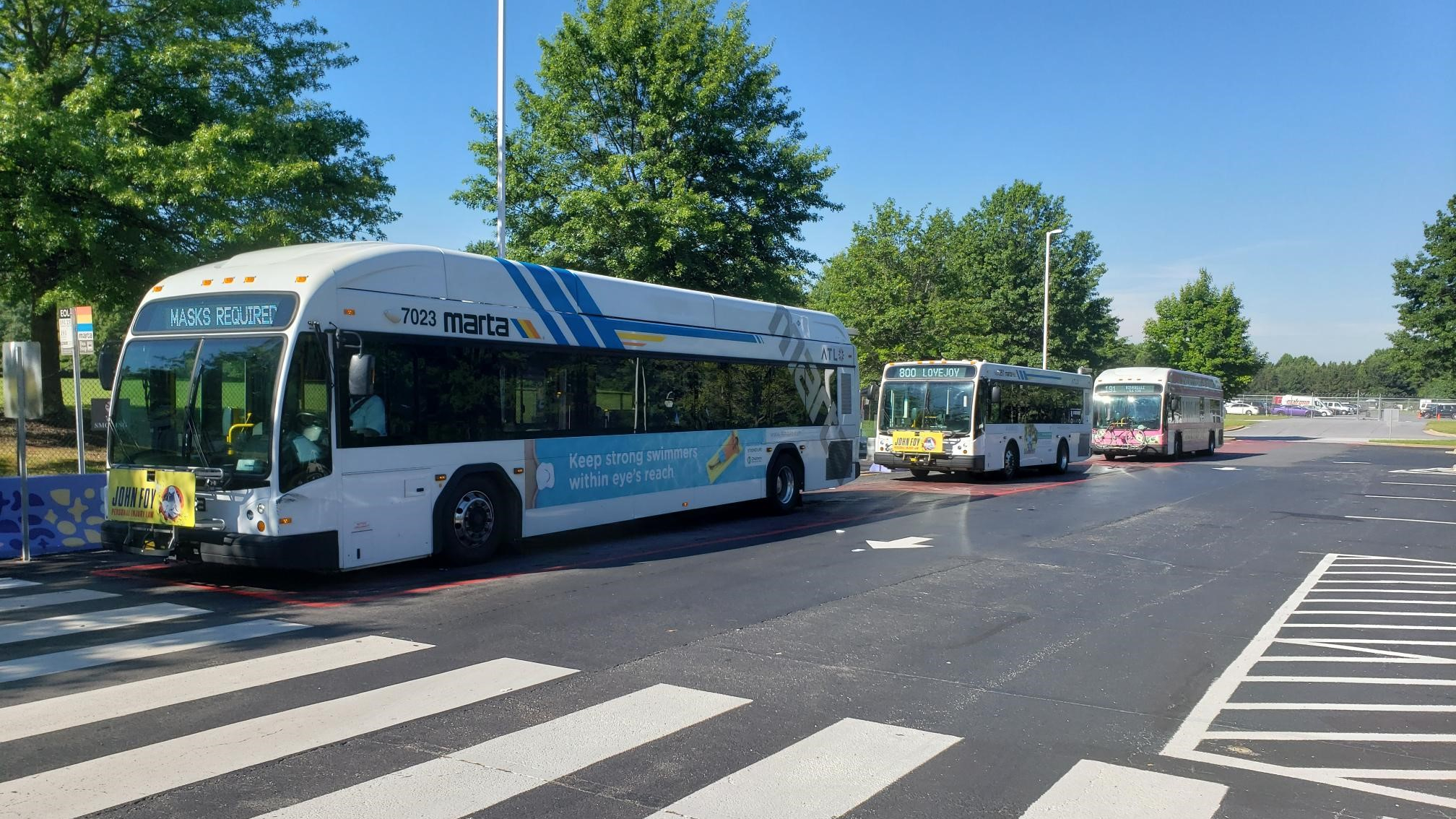 Three MARTA buses at a station with trees and clear skies.