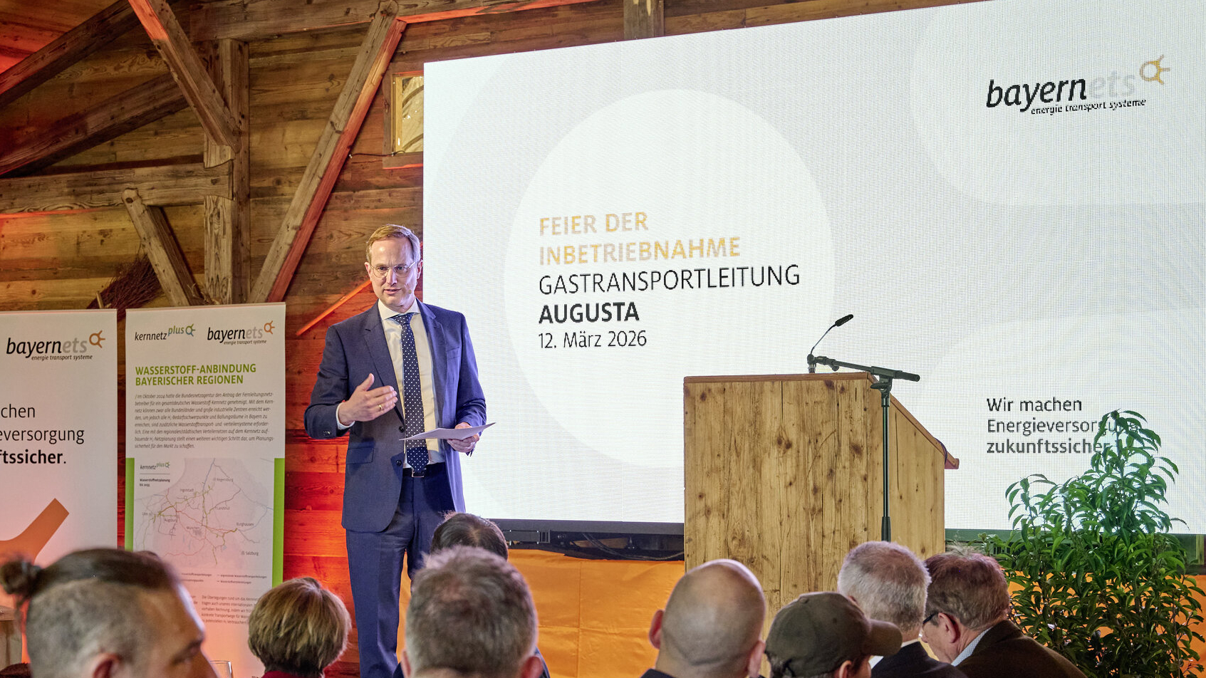 A speaker presents at a podium during a corporate event in a rustic indoor venue.