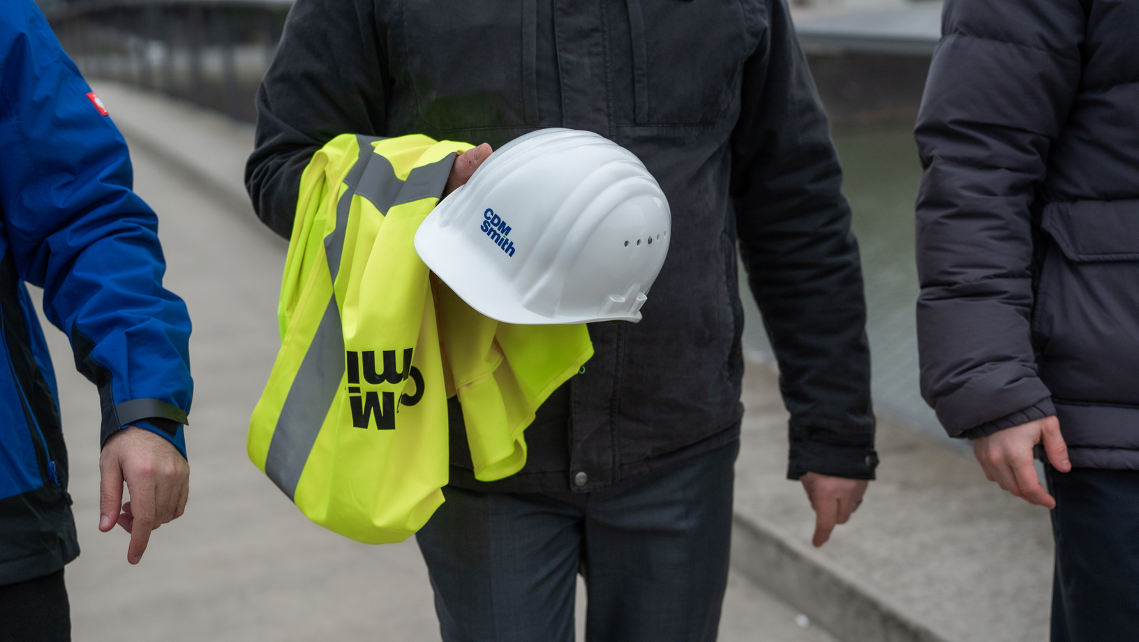 Person holding a white hard hat and yellow safety vest with "CDM Smith" logo.