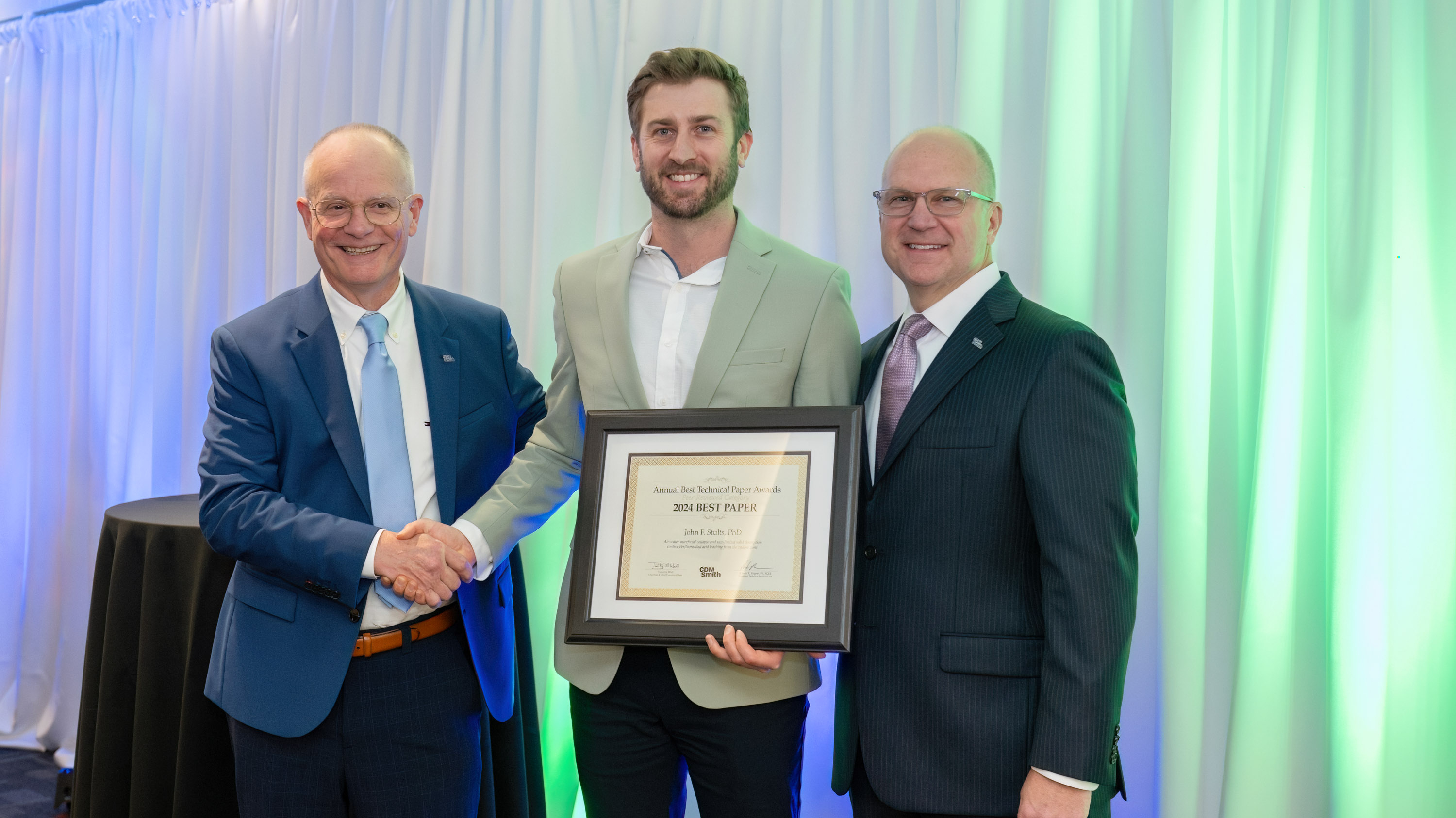 Three people at an awards ceremony, one holding a 2023 Best Paper award certificate, standing in front of a draped backdrop.