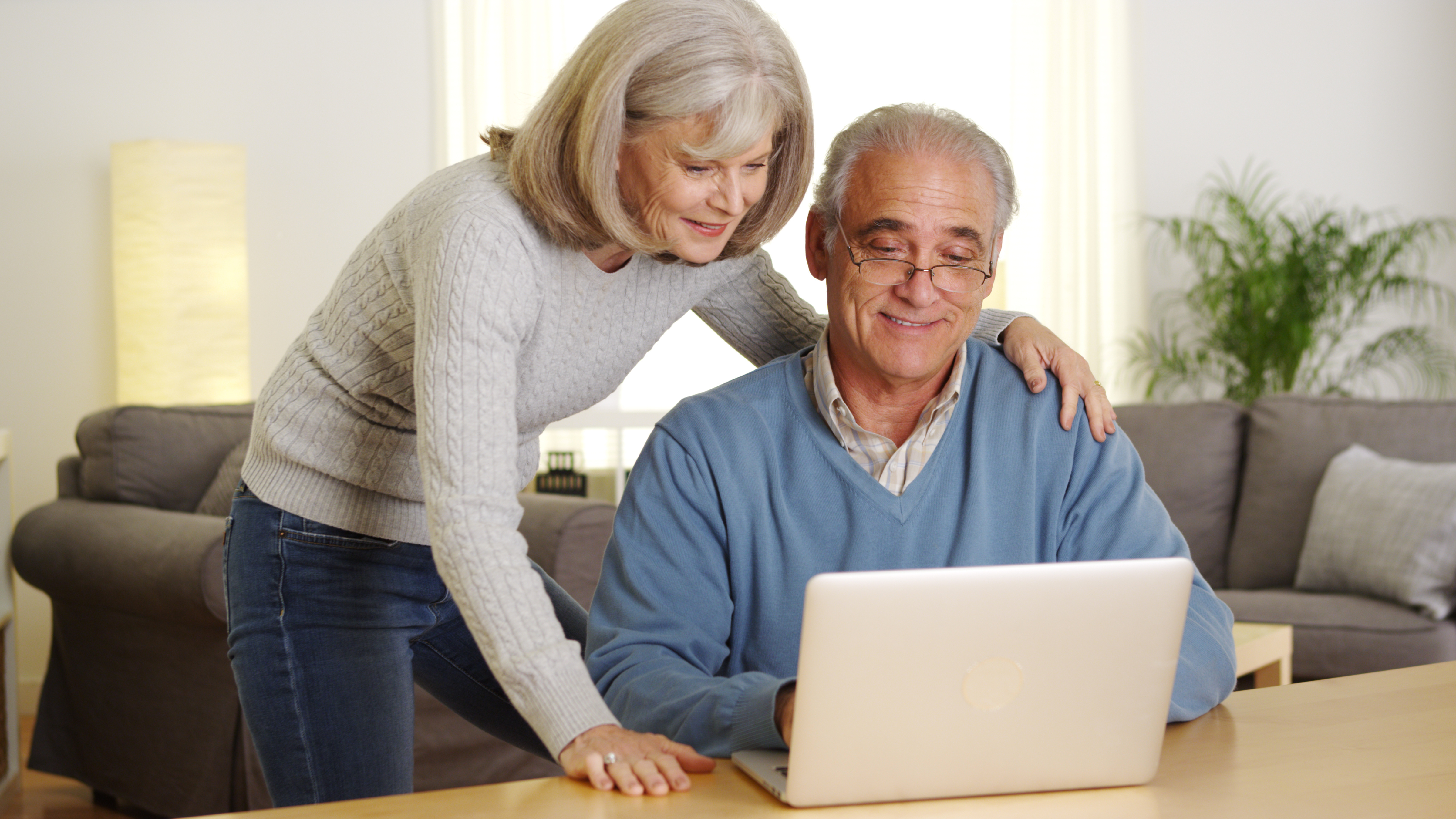 Older couple using a laptop at a table in a cozy living room.