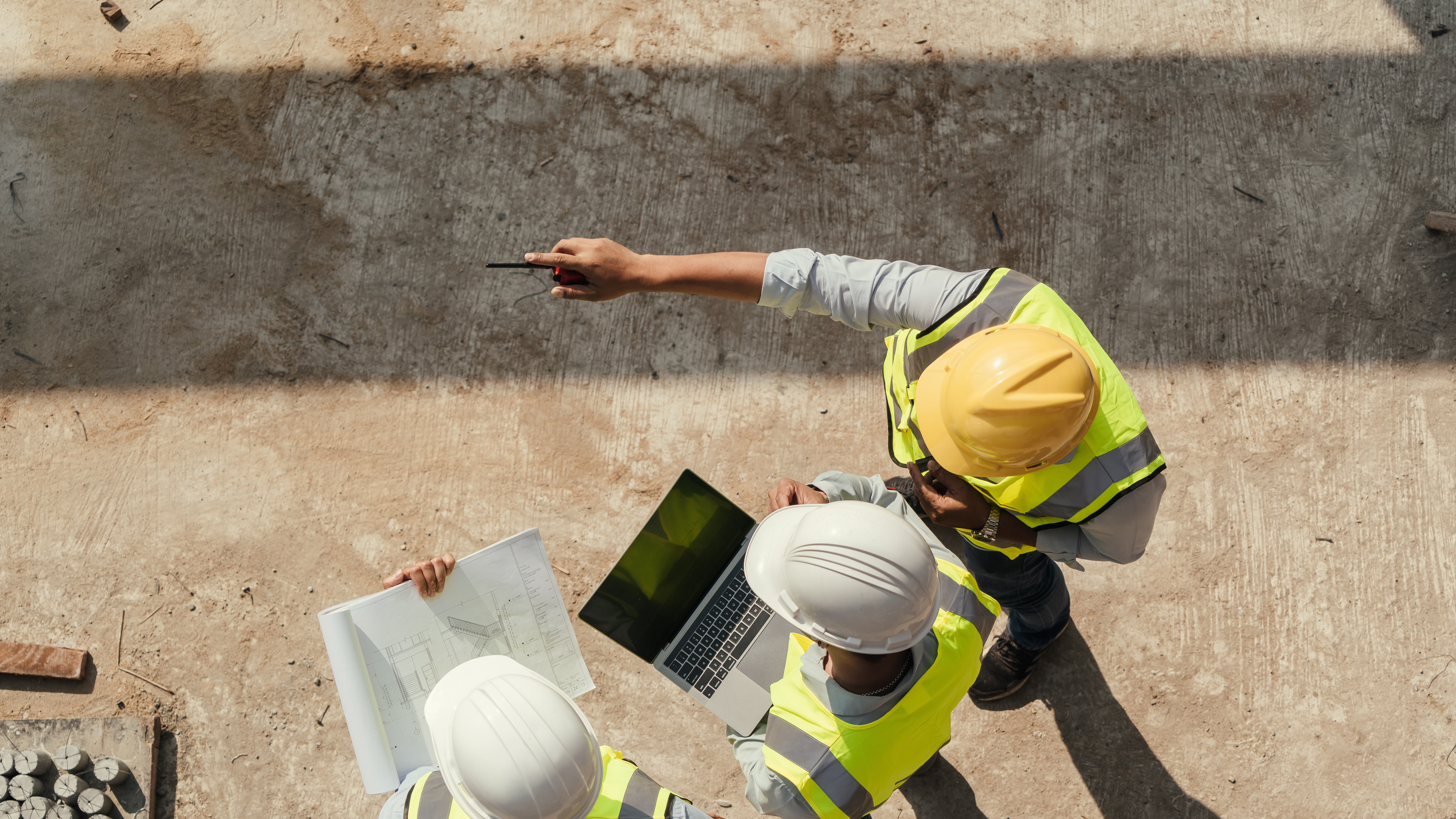 Drei Bauingenieur*innen mit Schutzkleidung überwachen die Baustelle