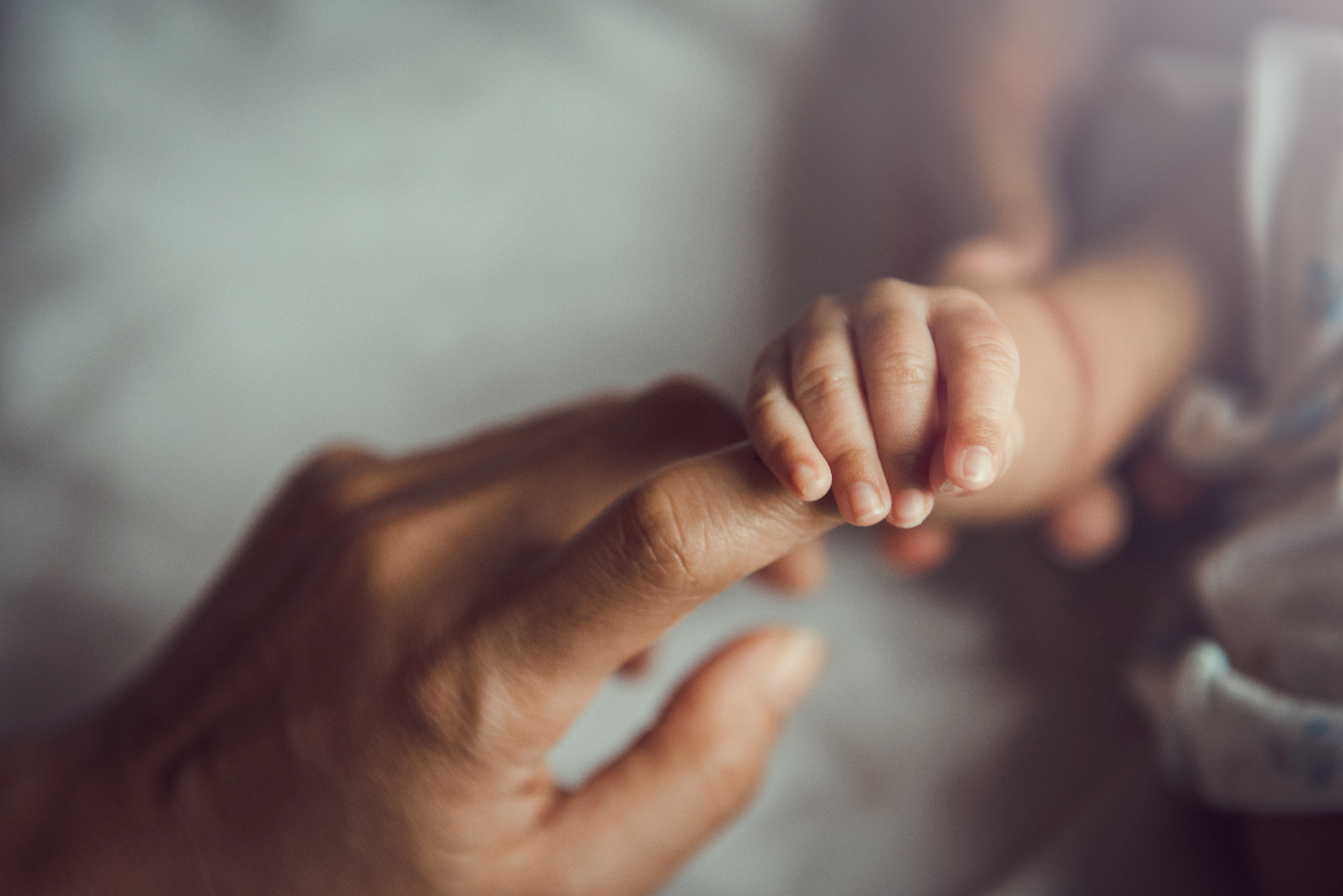 Close-up of a baby's hand gently holding an adult's finger, symbolizing care and connection.