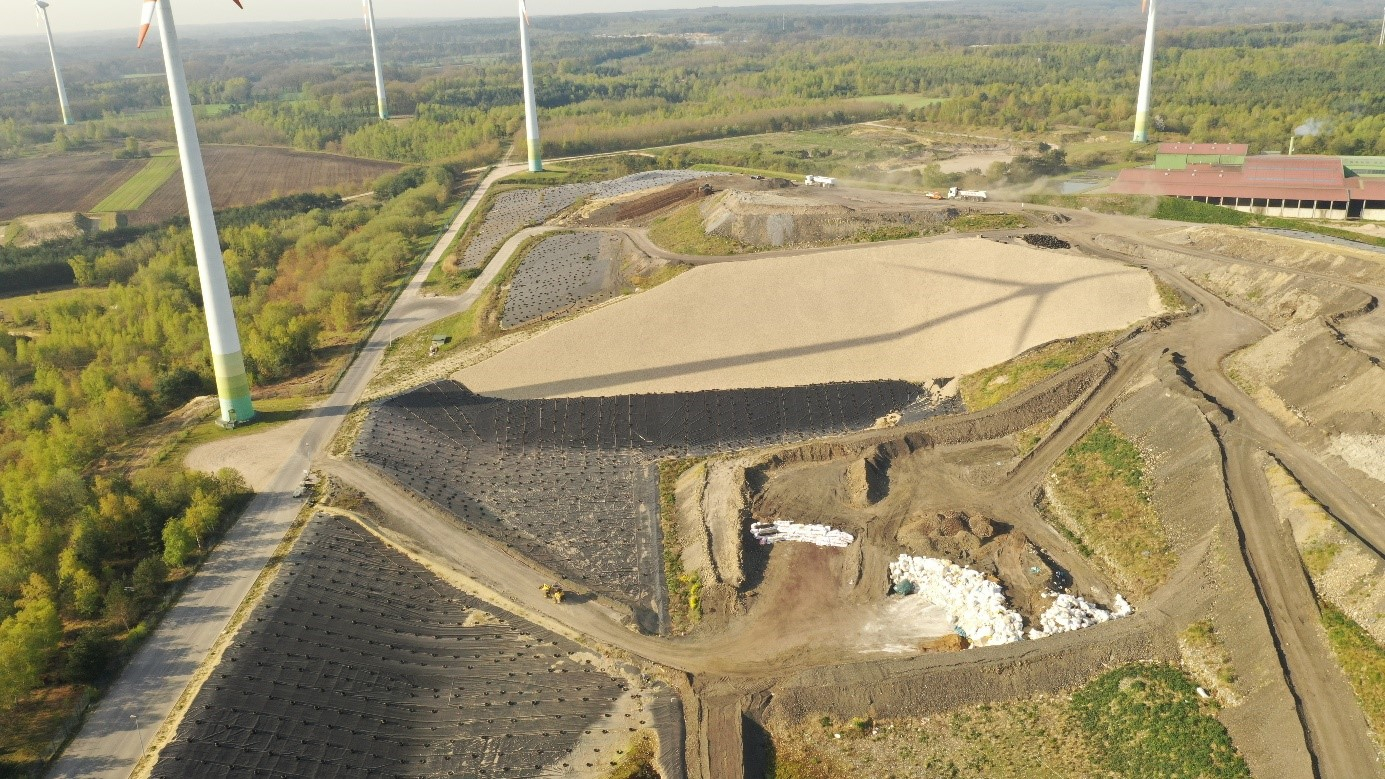 Aerial view of a landfill site with wind turbines and surrounding greenery.