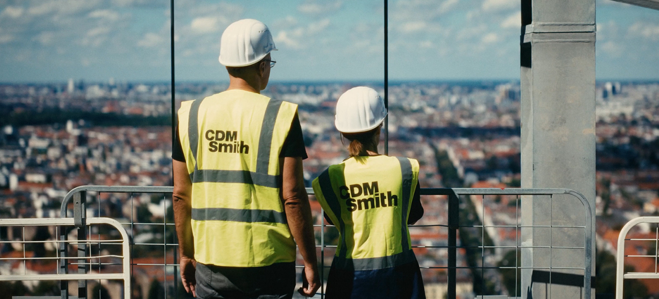 Two construction workers in safety gear overlooking a city skyline.