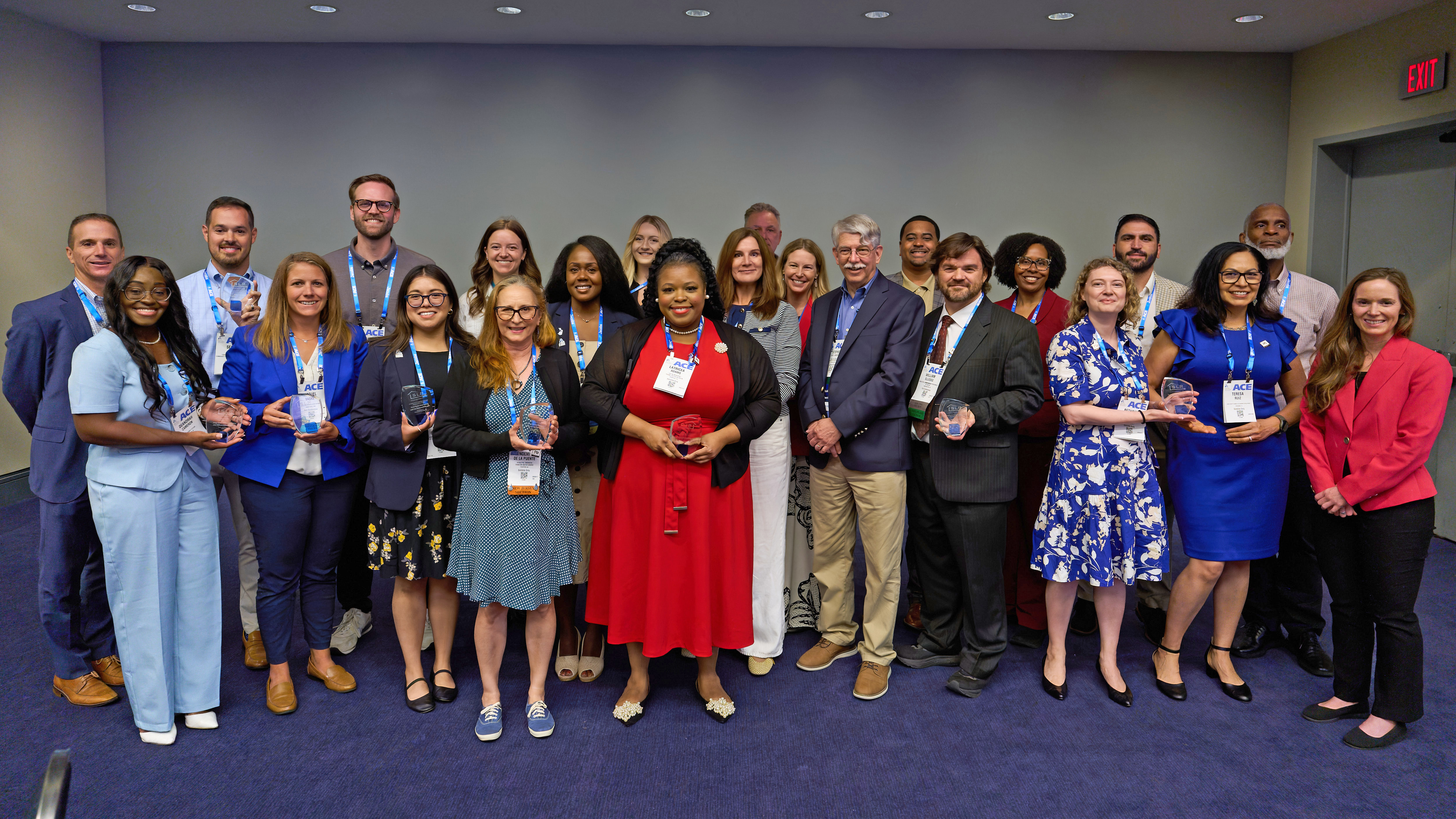 A group of individuals standing in a room, several holding awards and wearing conference badges, posing for a photo.